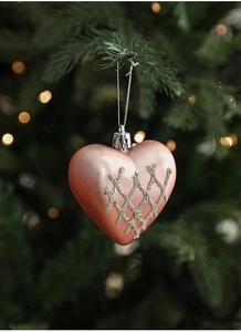 Pink heart-shaped Christmas ornament with silver glitter grid hanging on green tree branch