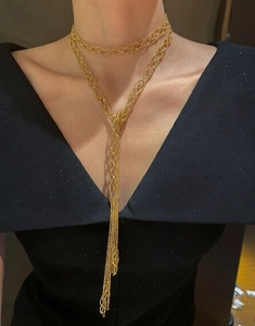Detail of gold mesh woven long tassel necklace on model wearing a black V-neck top