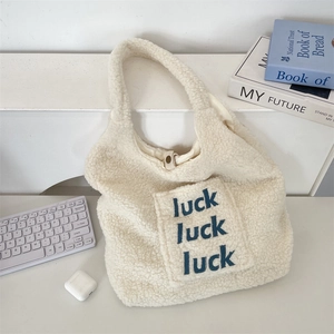 Macro detail of plush beige faux fur tote bag with blue luck letter embroidery and snap