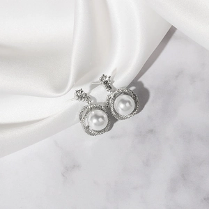 Macro view of French style pearl stud earrings with sparkling zircons on white silk background