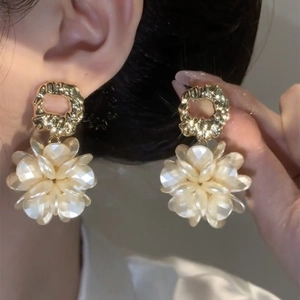 Detail of elegant gold-plated flower earrings with white petals on a model's ear