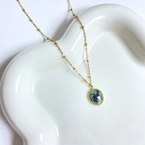 Detailed close-up of a 14K gold plated bohemian necklace with green stone on a white tray