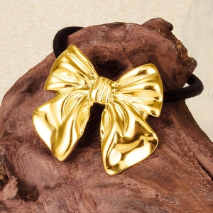 Close-up of golden bow hair tie made of 304 stainless steel on a rustic wood base