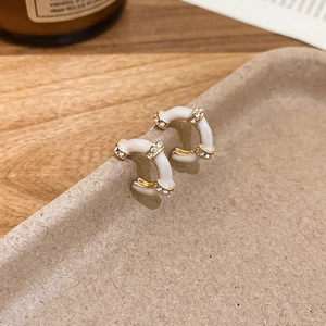 Detail of C-shaped white enamel earrings with gold plating and sparkling crystals