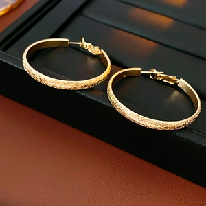 Nahaufnahme goldener Creolen mit matter Glitzertextur auf schwarzem Schmuckdisplay