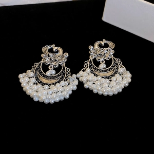 Macro shot of ethnic phoenix moon stud earrings with multiple white pearl tassels on velvet