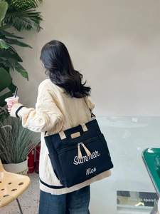 Close-up of black canvas tote bag with Summer embroidery and beige shoulder straps