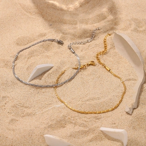 Close-up of gold and silver sparkling anklets with lobster clasps on a white sand background