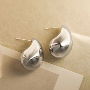 Elegante silberne Tropfenohrstecker mit polierter Metalloberfläche auf weichem Grund