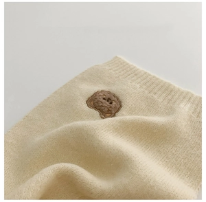 Close-up of fluffy cream knitted scarf featuring a 3D brown bear embroidery patch