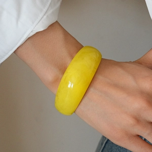 Close-up of a wide yellow resin bangle with a translucent finish on a person's wrist