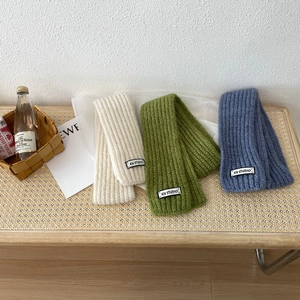 Detailed texture of knit scarves in beige, green, and blue with KN STUDIO woven labels