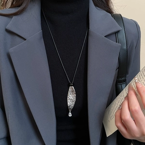 Close-up of a silver leaf pendant with hammer texture and crystal on a black cord