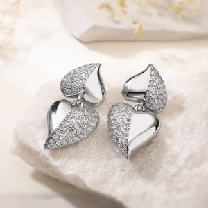 Silver-plated heart-shaped drop earrings with pavé zircons on stone background
