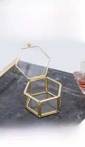 Close-up of hexagonal glass jewelry box with vintage brass metal frame on marble