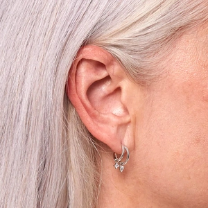 Close-up of minimalist silver hoop earrings with star and heart charms on model