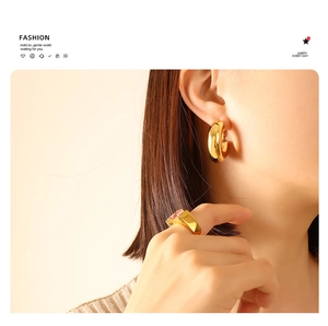 Close-up of minimalist gold U-shape earrings and a pink rectangle gemstone ring on a model