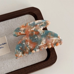 Close-up of marble pattern hair claw clip with star rhinestones on a wooden tray