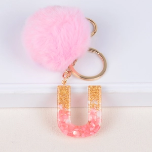 Detailed view of pink faux fur pompom keychain with resin letter U and gold foil