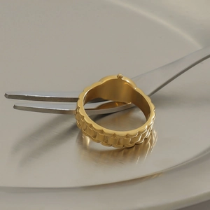 Makroaufnahme eines goldenen Edelstahlrings mit Wellentextur auf metallischem Display