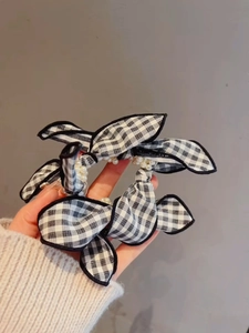Detail of checkered bow hair scrunchie with faux pearls held against a gray background