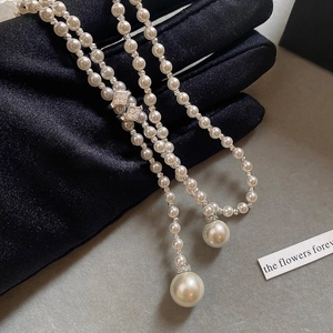 Close-up of pearl necklace with zircon-studded buckle and long tassel on black background