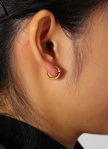 Macro view of gold hoop earring with blue zircon inlay on model's earlobe