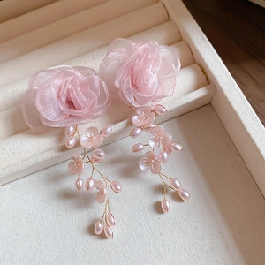 Macro detail of pink fabric flower earrings with pearl tassels on a jewelry tray