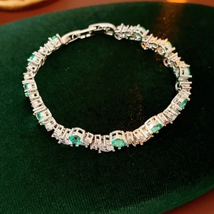 Detailed macro of silver tennis bracelet with green emerald stones and zircon accents