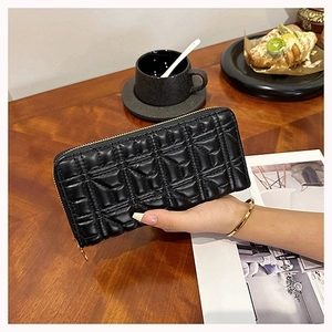 Close-up of black quilted long wallet for women being held over a wooden table setting