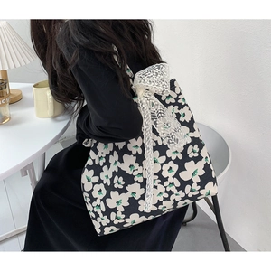 Detailed close-up of canvas tote bag with floral print and lace bow on female model