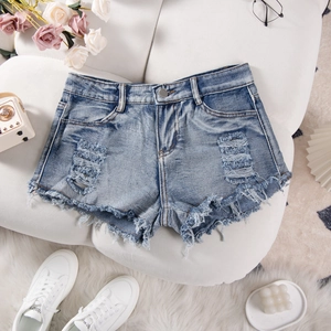 Flat lay of distressed denim shorts with ripped details and raw hem on white fabric