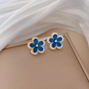Detailed macro view of gold-tone five-petal flower stud earrings with blue drop-shaped stones