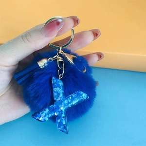 Blue pompom keychain with glitter letter X and gold hardware shown in hand for scale
