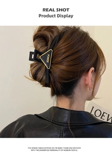 Detail view of a black and gold triangular hair claw clip with POWER text on a model