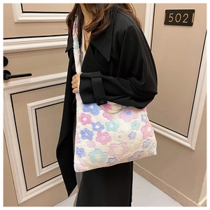 White plush tote bag with colorful flower patterns worn by a model in a black jacket