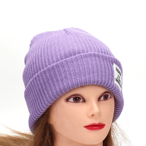 Detail of purple ribbed knit beanie with vertical texture and white patch on a model