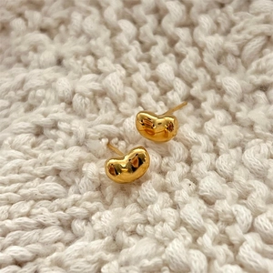 Macro shot of gold bean earrings on a beige knit background with polished finish