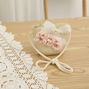 Détail d'un sac en paille pour enfant avec fleurs en mousseline et nœud blanc