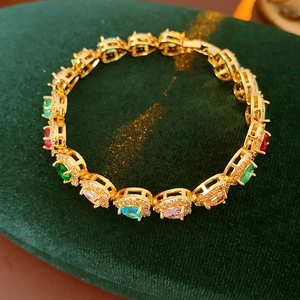 Detail of elegant gold bracelet with colorful cubic zirconia on dark green velvet