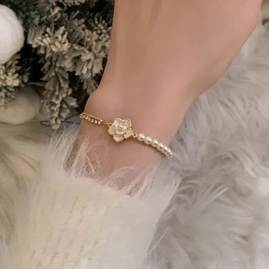 Detailed view of elegant camellia bracelet with pearls on a model wearing white sweater
