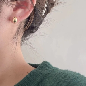 Macro shot of minimalist gold bean-shaped silver earring worn by model in green sweater
