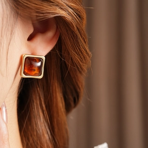 Detailed close-up of vintage resin amber earring in square metal frame on model