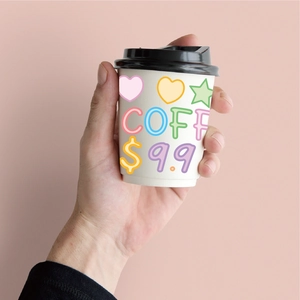 Close-up of a white paper coffee cup featuring colorful hearts and star patterns