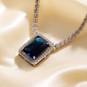 Close-up of luxury necklace with emerald-cut blue gemstone and halo of white zircons