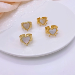 Macro detail of four vintage gold-plated heart rings with white shell inlays on a ceramic tray