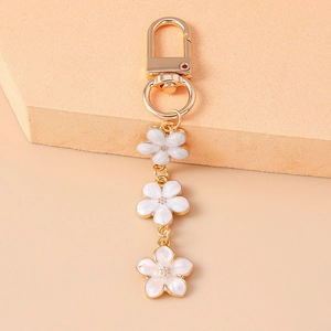 Close-up of white enamel cherry blossom flowers with gold metal plating on keychain