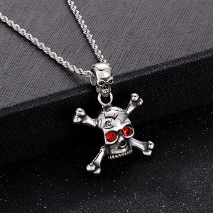 Macro detail of silver bone pendant with red crystal eyes on a black textured surface