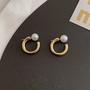 Macro shot of gold C-shaped earrings with elegant white pearls on dark texture