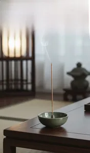 Macro detail of celadon ceramic incense burner with a burning stick in Zen setting